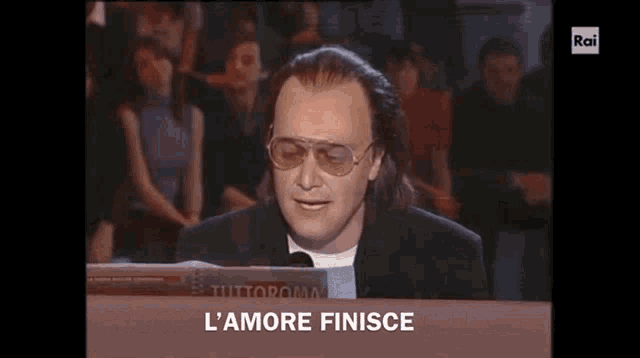 a man wearing sunglasses is sitting at a keyboard in front of a crowd and says l ' amore finisce .