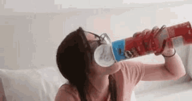a woman wearing glasses is drinking from a can of soda .