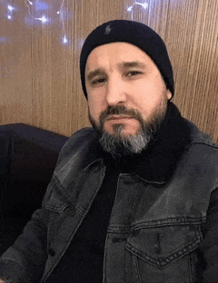 a man with a beard is wearing a black hat and a denim jacket