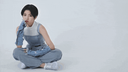 a woman sits on the floor with her legs crossed and a blue background behind her