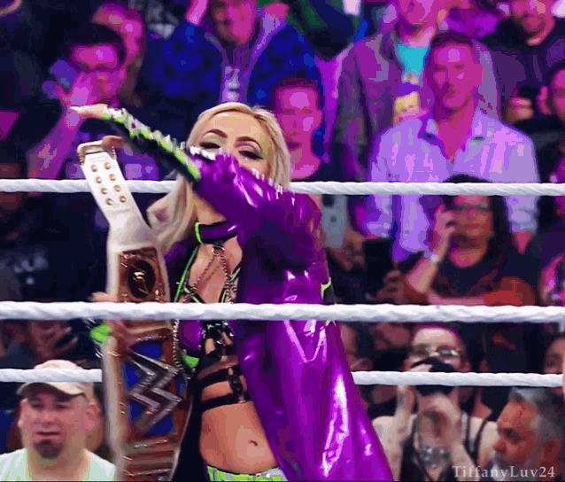 a woman in a purple and green outfit is holding a wrestling championship belt