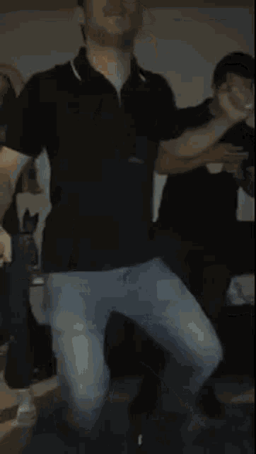 a man in a black shirt and blue jeans is standing in front of a table .