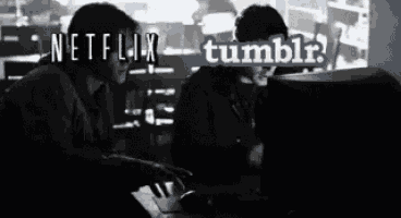 a black and white photo of two people looking at a computer screen with the words netflix and tumblr visible .
