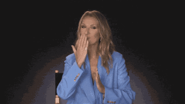 a woman in a blue jacket is sitting in a chair and waving her hand
