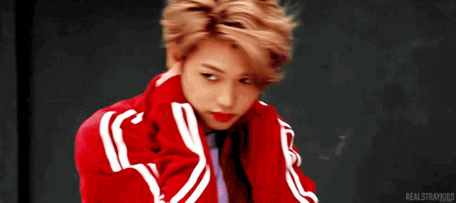 a young boy wearing a red jacket with white stripes on the sleeves is standing in front of a black wall .