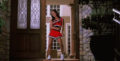 a cheerleader is standing in front of a door wearing a red skirt .