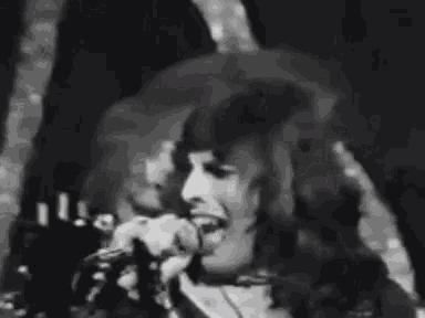 a black and white photo of a man with long hair making a face .