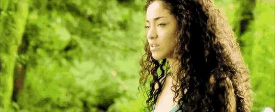a woman with curly hair is standing in front of a forest .