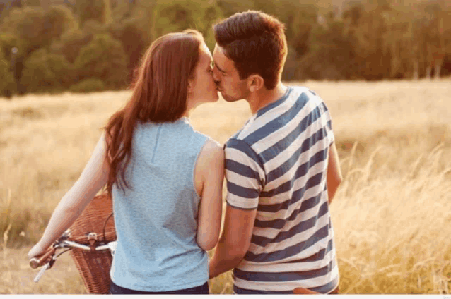 a man and a woman kissing in a field with a bicycle