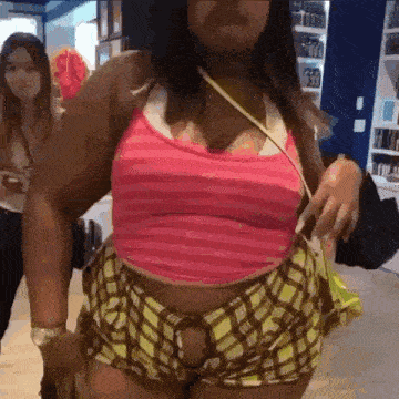 a woman in a pink tank top and yellow shorts is standing in a store .