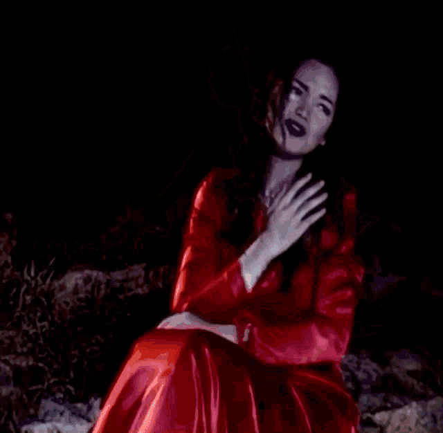 a woman in a red dress sits on a rock with her hands in the air