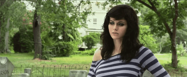 a woman in a striped shirt is standing in front of a cemetery with a gravestone that says johnson