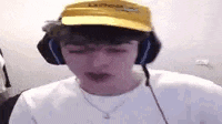 a man wearing headphones and a yellow hat is sitting in front of a computer screen .