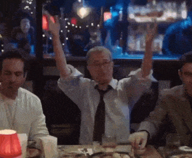 a man is sitting at a table with his arms in the air .
