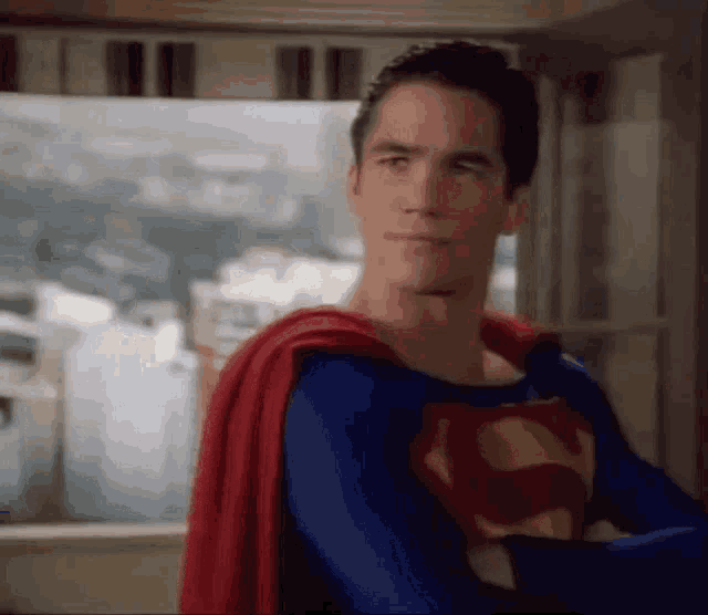 a man in a superman costume is standing in front of a window in a room .