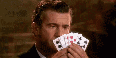 a man in a suit and tie is holding a hand of playing cards in his hands .