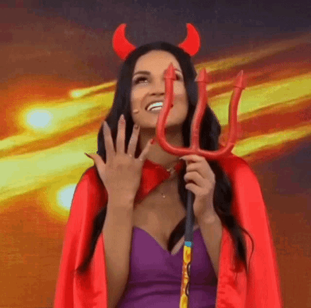 a woman in a devil costume is holding a trident and making a funny face .