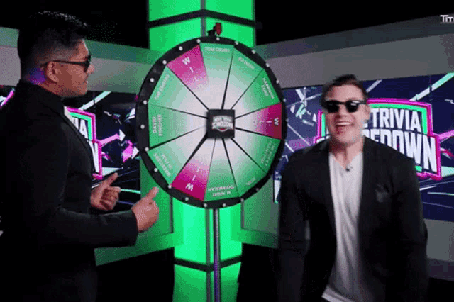 a man in sunglasses stands in front of a wheel that has the word trivia on it