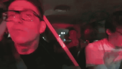 a man wearing glasses is sitting in the back seat of a car with another man .