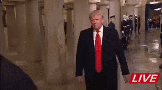 a man in a suit and tie is walking down a hallway with the word live on the bottom