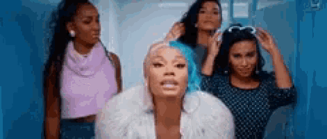 a group of women are standing next to each other in a hallway . one of the women has blue hair .