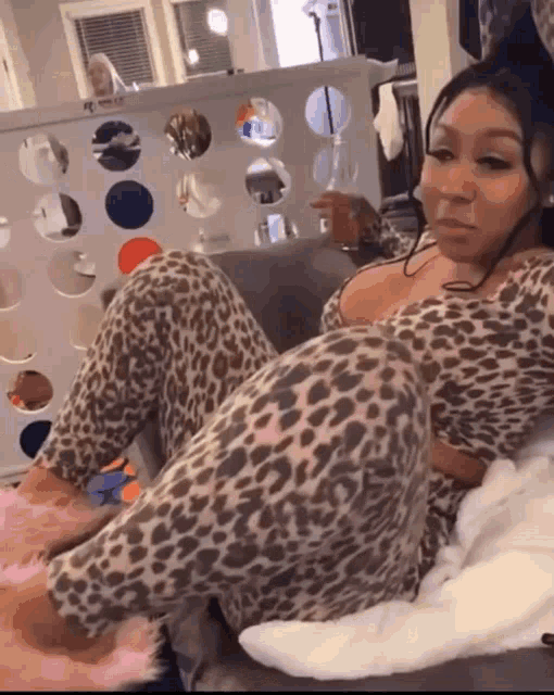 a woman in leopard print pajamas sits on a couch with her legs crossed