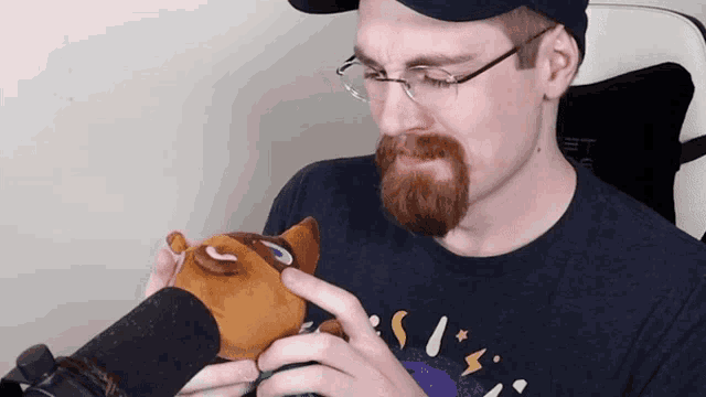 a man with glasses and a beard is holding a stuffed animal in his hands