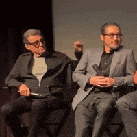 two men are sitting in chairs on a stage and one is holding a microphone