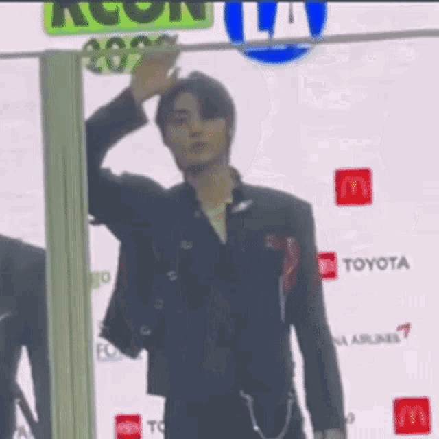 a man in a black jacket is standing in front of a sign that says toyota on it .