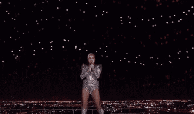 a woman in a silver outfit is dancing on a stage in front of a starry sky .