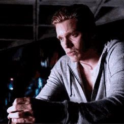 a man in a grey hoodie is sitting at a table in the dark .