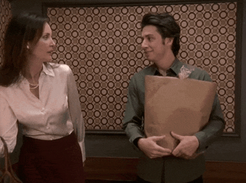 a man holding a brown paper bag stands next to a woman in front of a wall with circles on it