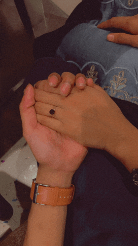 a man wearing a watch is holding a woman 's hand with a ring on her finger