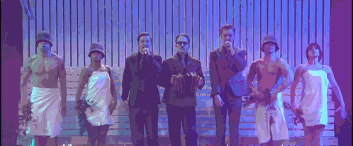 a group of people are standing on a stage and one of them is wearing a towel around his waist