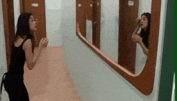 a woman is standing in a hallway looking at herself in a mirror .