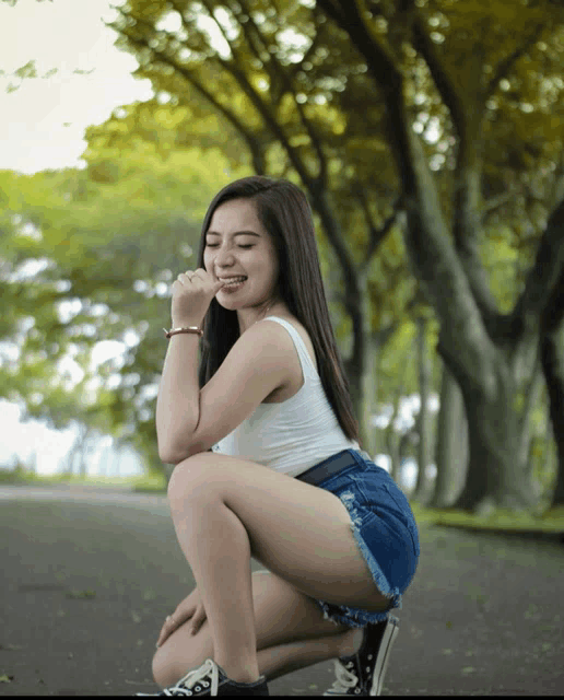 a woman in shorts and a white tank top is squatting down and smiling