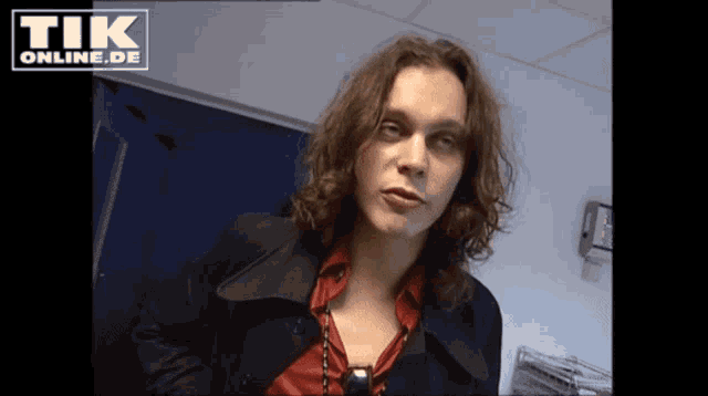 a man with long hair is standing in front of a sign that says tik online de