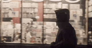 a man in a hoodie is walking past a store window .