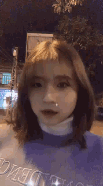 a girl with short hair is wearing a purple sweater and taking a selfie at night .