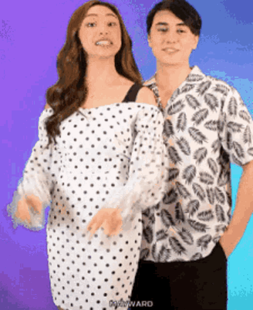 a woman in a polka dot dress is standing next to a man in a feather print shirt .