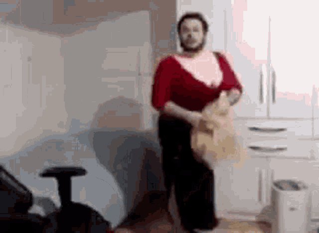 a man in a red shirt and black pants is standing in a room holding a bag .