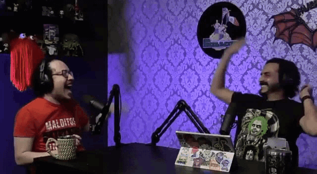 a man wearing a red shirt that says maldito laughs in front of a microphone