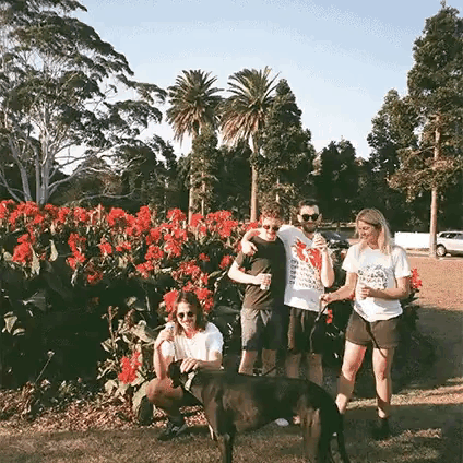 a group of people posing for a picture with a dog in front of a field of red flowers .