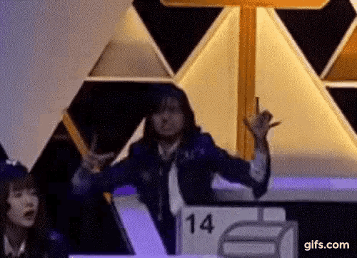 a woman is giving a peace sign while sitting at a table with a number 14 on it .