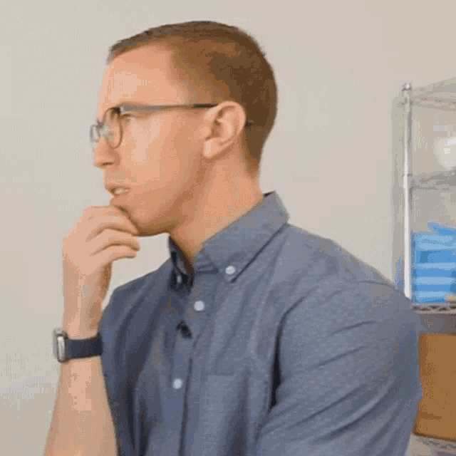 a man wearing glasses and a blue shirt looks to his left