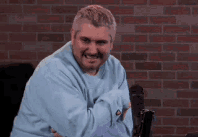a man in a blue sweater is sitting in front of a brick wall