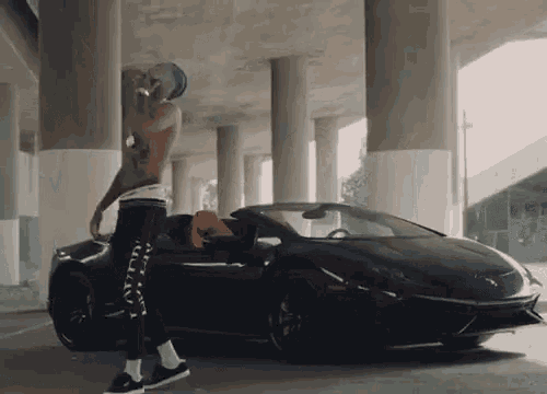 a man without a shirt is standing in front of a black car .