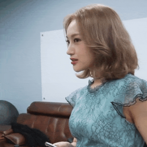a woman in a blue dress is sitting on a couch holding a cell phone