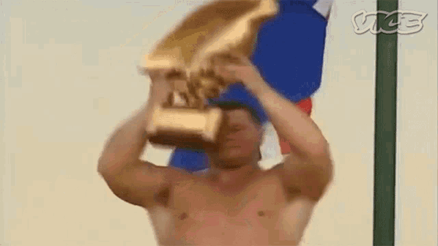 a shirtless man is holding a gold trophy over his head .