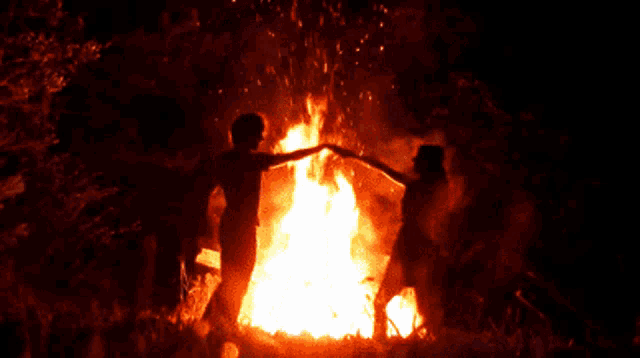 a couple dancing in front of a large fire